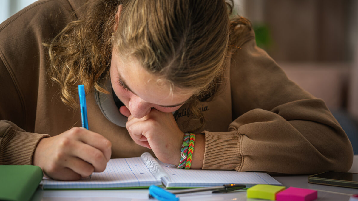 Schoolgirl with poor eyesight writing with face close to the notebook doing a school assignment at home
