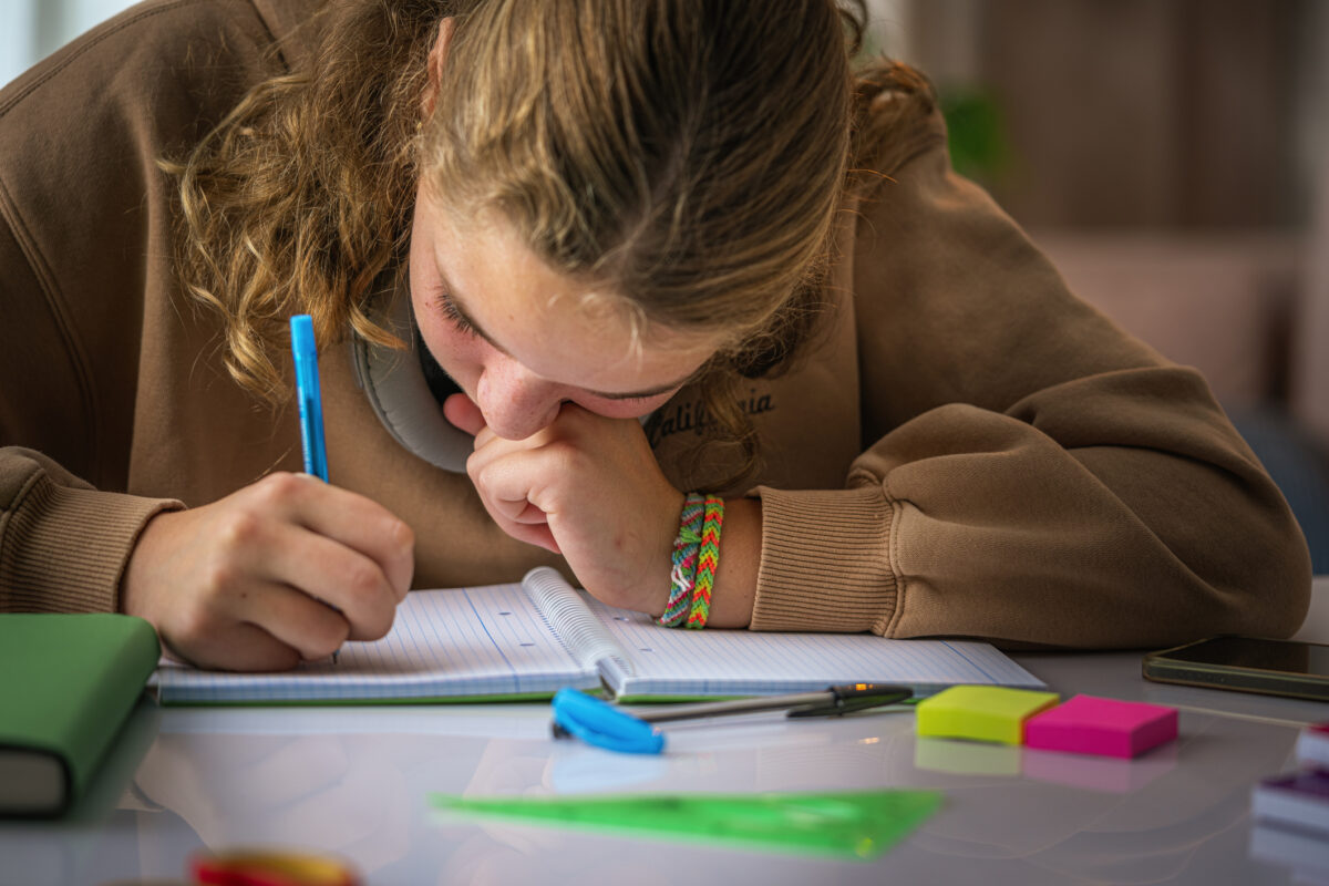 Schoolgirl with poor eyesight writing with face close to the notebook doing a school assignment at home