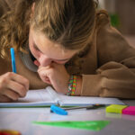 Schoolgirl with poor eyesight writing with face close to the notebook doing a school assignment at home