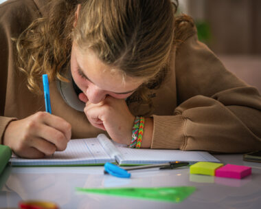 Schoolgirl with poor eyesight writing with face close to the notebook doing a school assignment at home