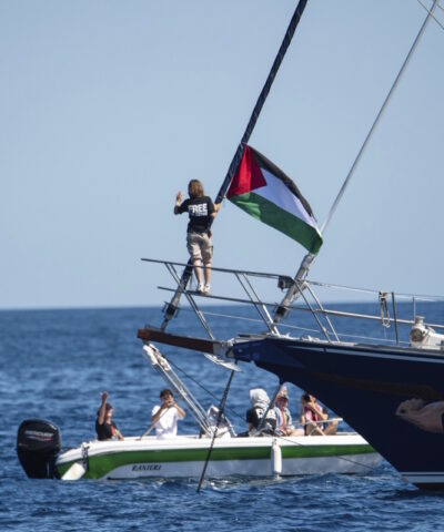 Η ακτιβίστρια για το κλίμα Γκρέτα Τούνμπεργκ στέκεται δίπλα σε παλαιστινιακή σημαία μετά την επιβίβασή της στο πλοίο Madleen και πριν αποπλεύσει για τη Γάζα μαζί με ακτιβιστές του Συνασπισμού Στόλου της Ελευθερίας