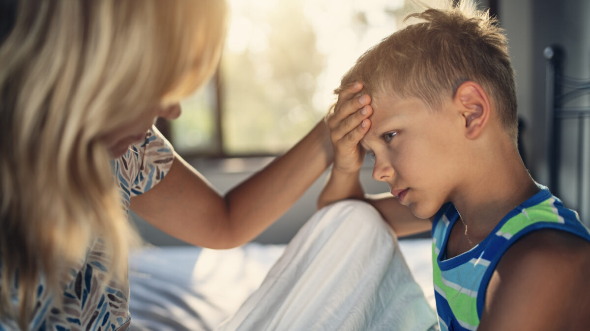 Sick little boy sitting on bed. The boy has a head ache and fever. The mother is comforting the boy.