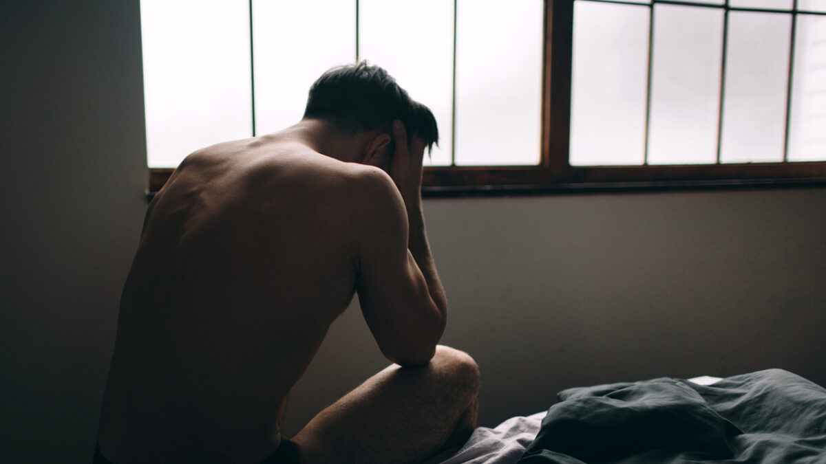 Depressed man sitting on bed in an empty room. This is major depressive disorder.