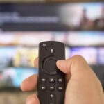 Male hand holding the TV remote control and changing TV channels. Channel surfing, focused on the hand and remote control. Internet TV.