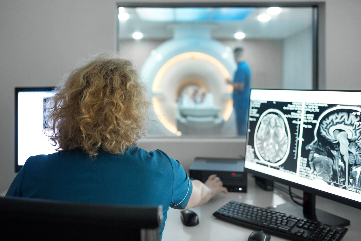 Closeup rear view of a female technicians during MRI scanning procedure discussing images in the control room.