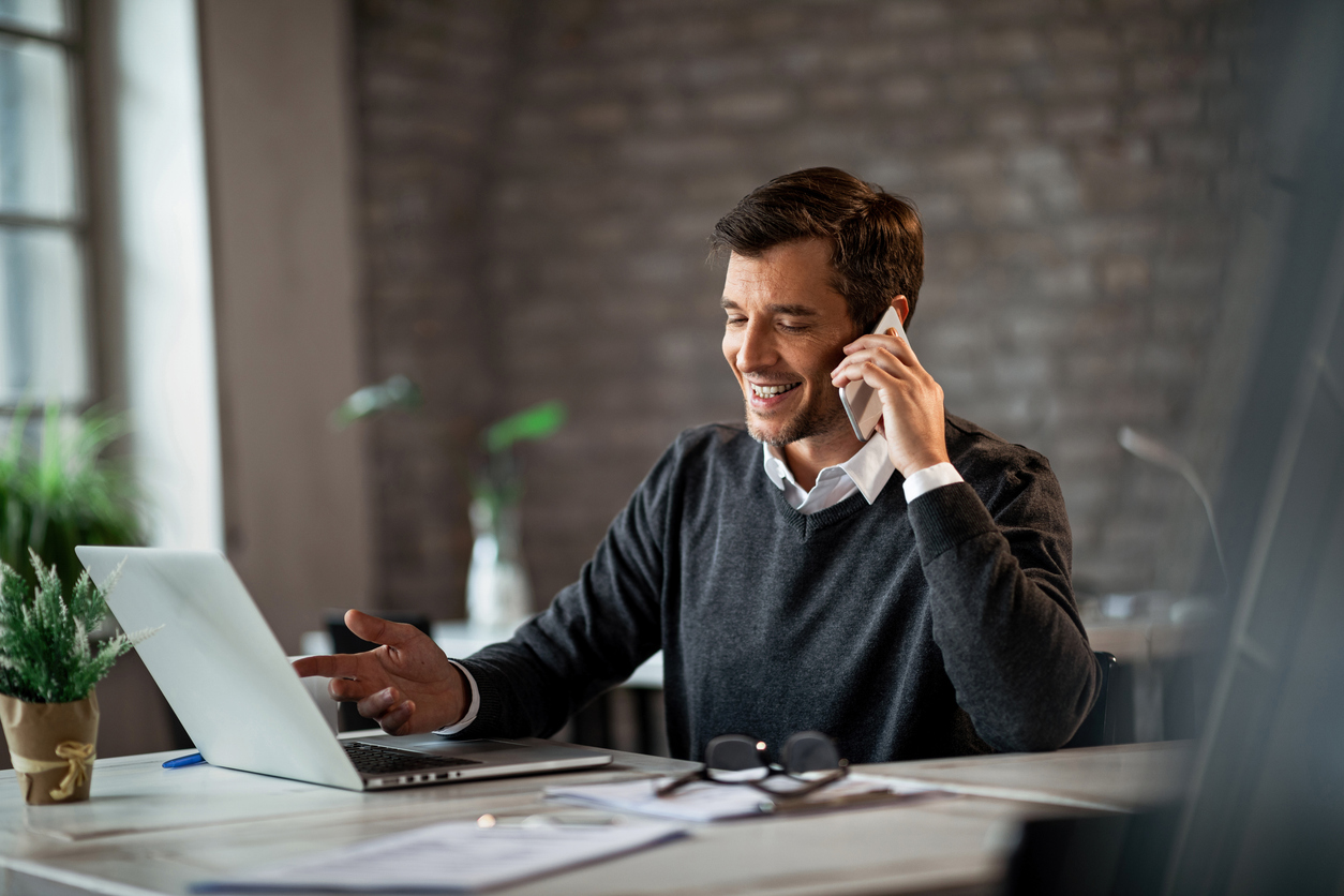 Happy businessman communicating over mobile phone and working on laptop while being at work