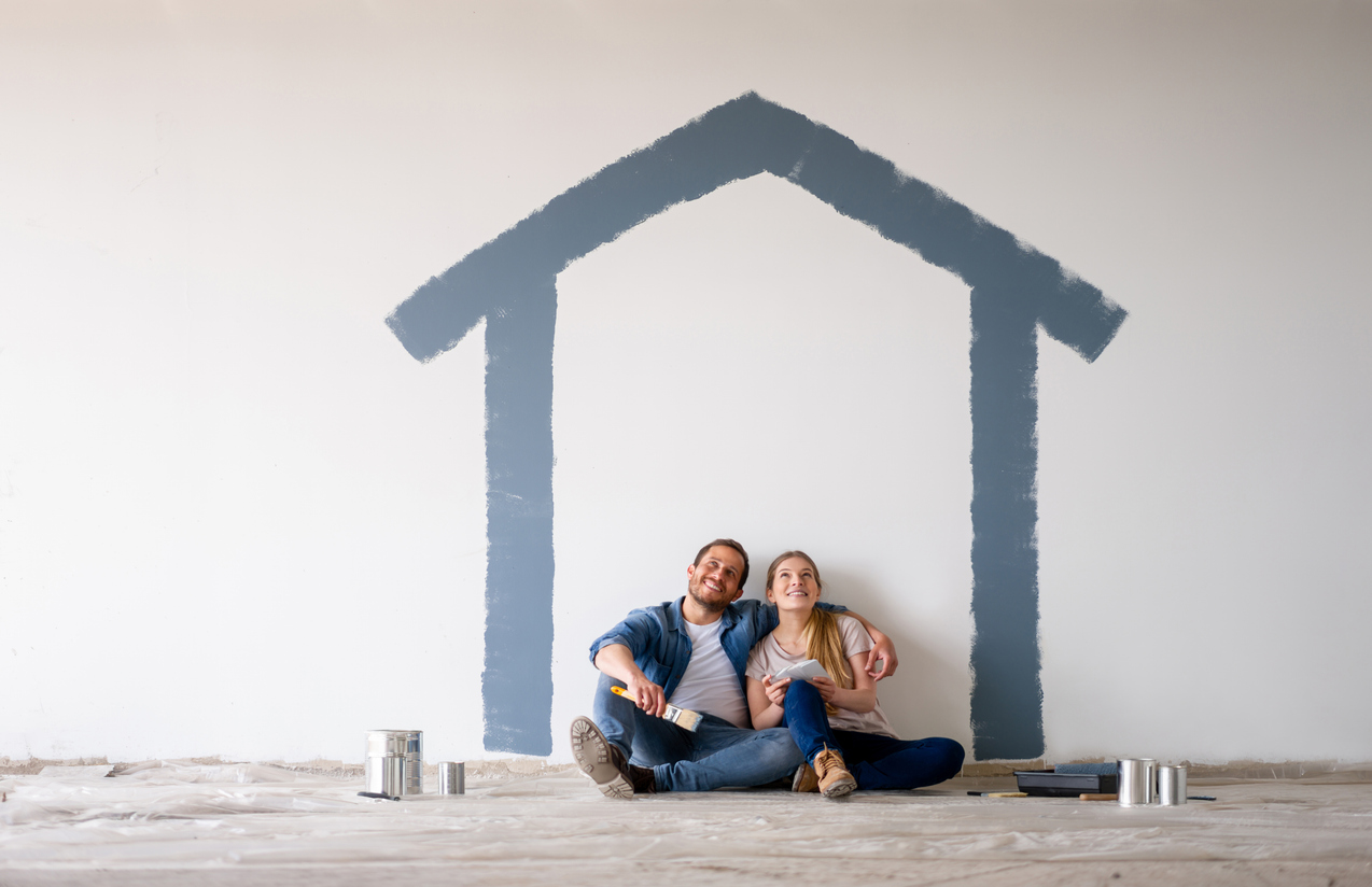 Happy Latin American couple painting their house and daydreaming about how it's going to look when finished - home improvement concepts