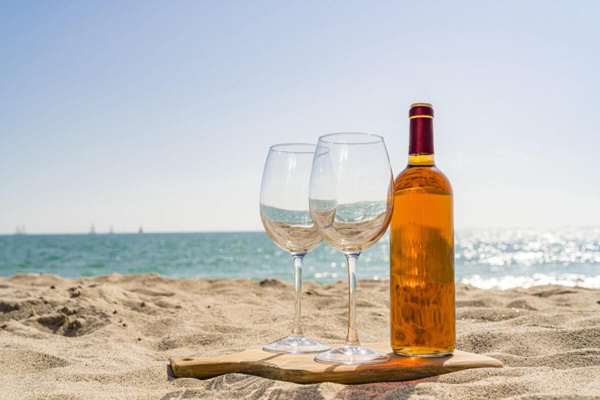 Rose wine bottle and two wineglasses on beach sand. High resolution 42Mp outdoors digital capture taken with SONY A7rII and Zeiss Batis 40mm F2.0 CF lens