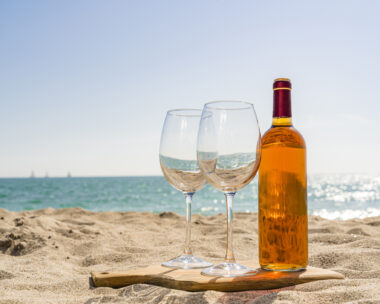 Rose wine bottle and two wineglasses on beach sand. High resolution 42Mp outdoors digital capture taken with SONY A7rII and Zeiss Batis 40mm F2.0 CF lens