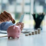 Hands of a young Asian businessman Man putting coins into piggy bank and holding money side by side to save expenses A savings plan that provides enough of his income for payments