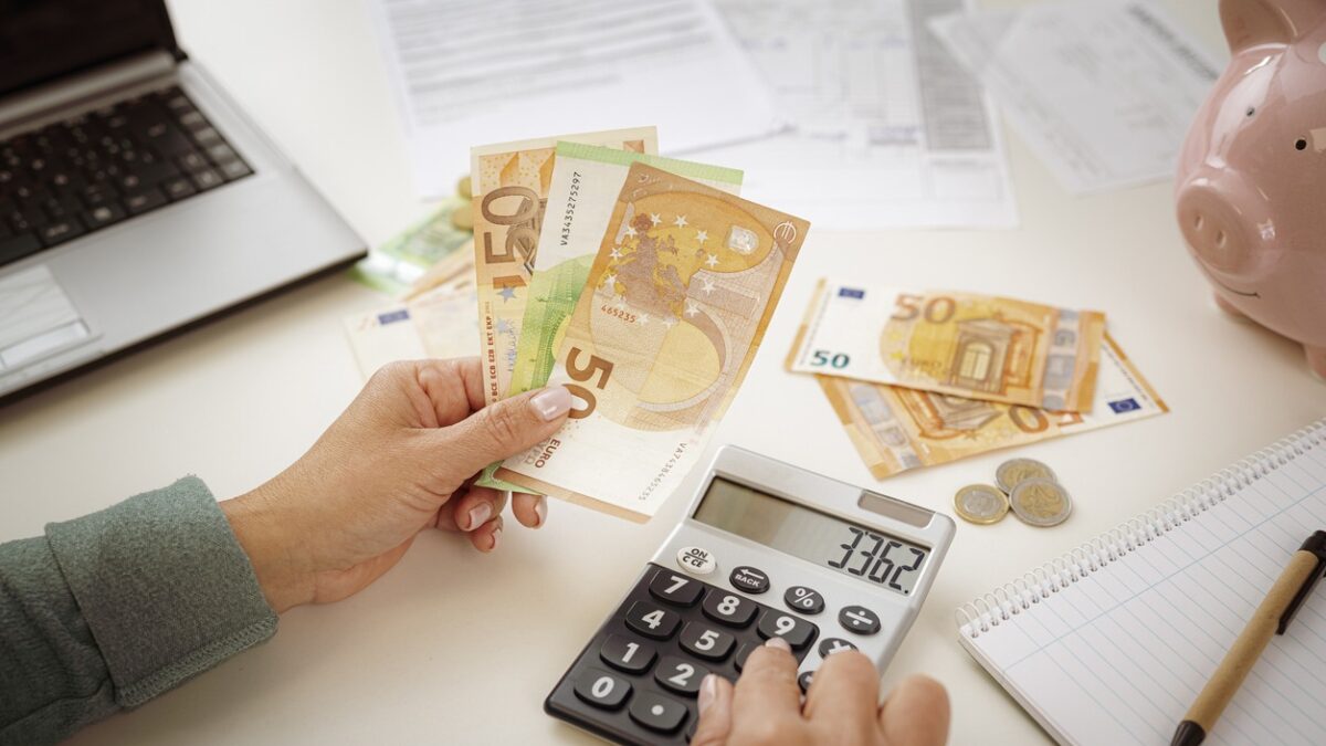 Close-up of woman's hands using calculator for planning home finances. She is holding Euro banknotes