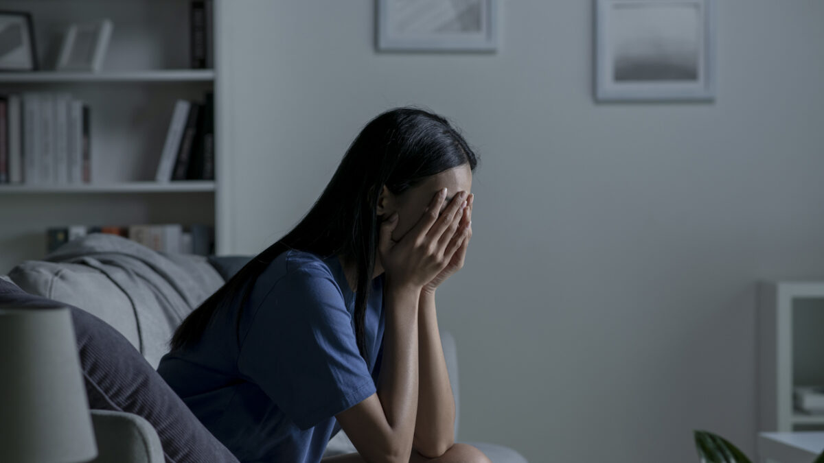 Young Asian woman sitting on sofa at home feeling sad tired and worried suffering depression in mental health.