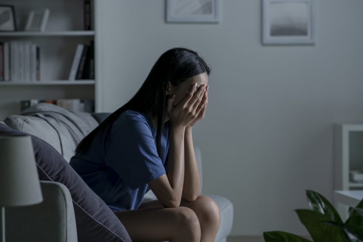 Young Asian woman sitting on sofa at home feeling sad tired and worried suffering depression in mental health.