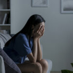 Young Asian woman sitting on sofa at home feeling sad tired and worried suffering depression in mental health.