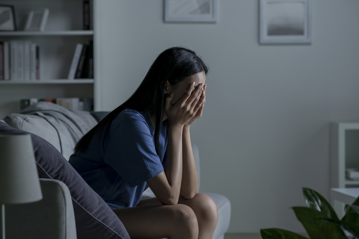 Young Asian woman sitting on sofa at home feeling sad tired and worried suffering depression in mental health.