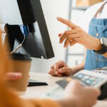 Woman cashier wears an apron and using pos terminal to payment for credit card on coffee shop counter