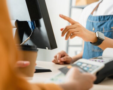 Woman cashier wears an apron and using pos terminal to payment for credit card on coffee shop counter
