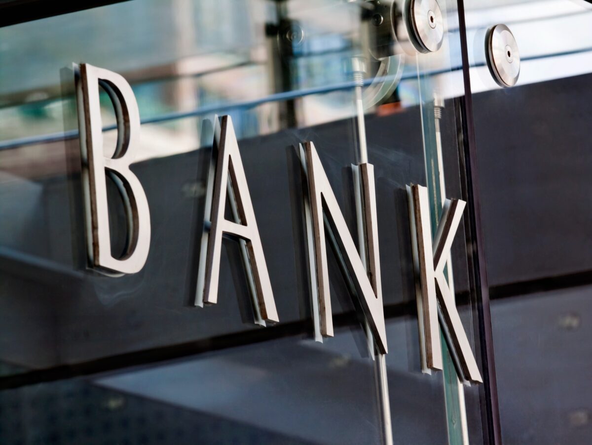 Modern metal Bank sign lettering fixed to a glass wall, with reflections in the glass