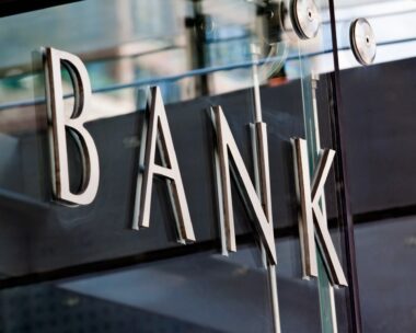 Modern metal Bank sign lettering fixed to a glass wall, with reflections in the glass