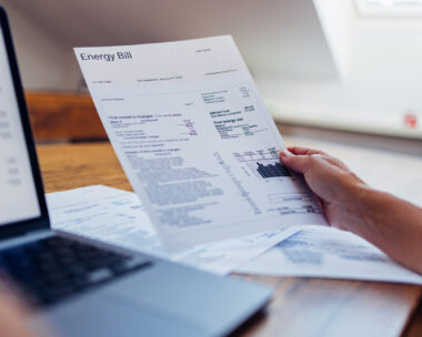 A person reviews their energy bill while using a laptop at home. The document includes various charges and electricity usage information.