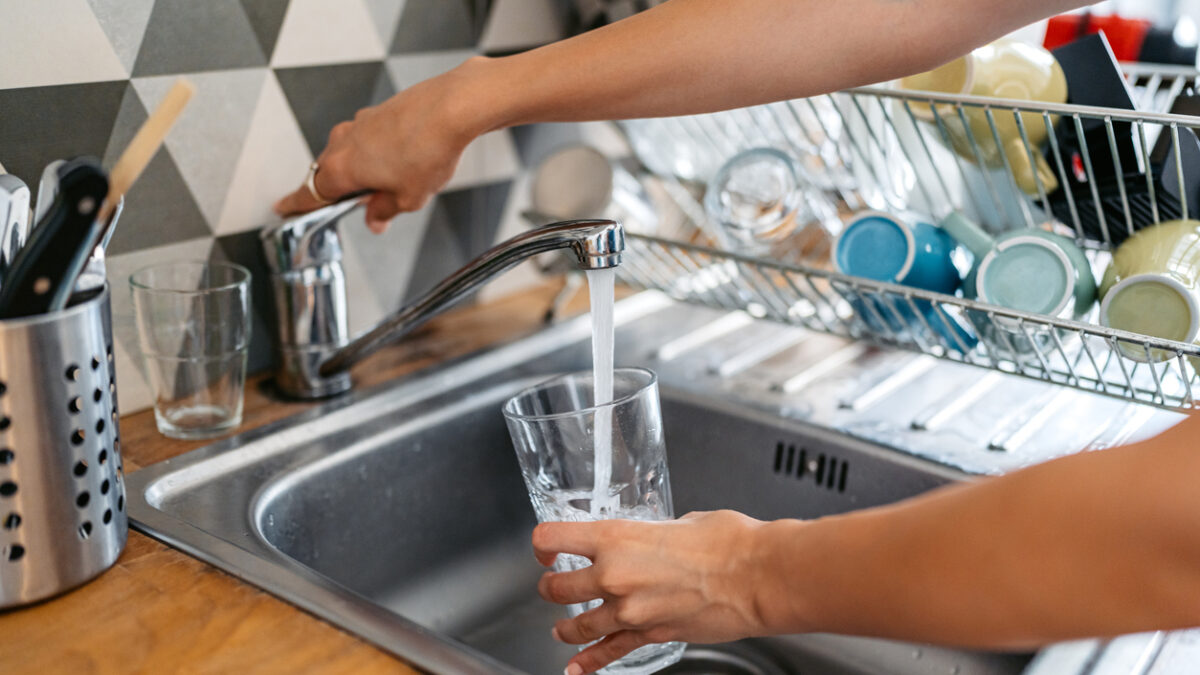 Young woman filling a glass of water in the sink. Close-up.