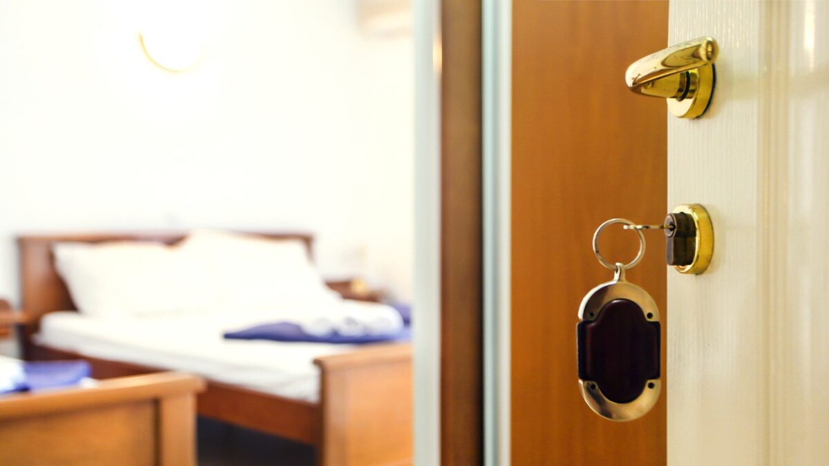 Key in keyhole with bedroom in the background in a hotel or apartment (travel or real estate concept)