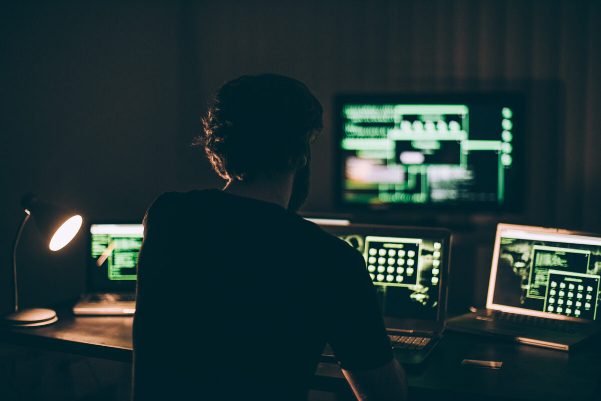 One hacker sitting in the dark room in front of his computers, hacking some internet data.