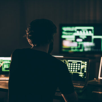 One hacker sitting in the dark room in front of his computers, hacking some internet data.