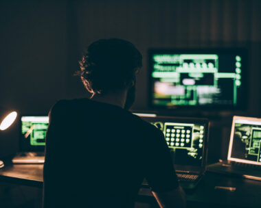 One hacker sitting in the dark room in front of his computers, hacking some internet data.