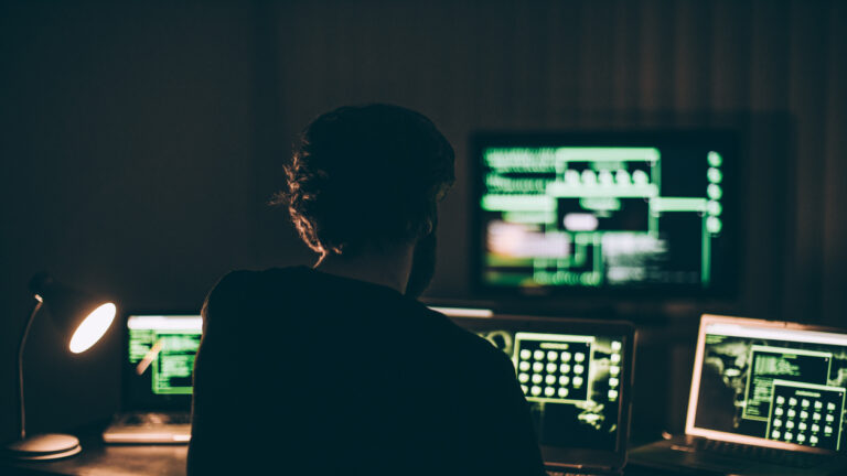 One hacker sitting in the dark room in front of his computers, hacking some internet data.