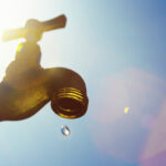 A single droplet falls from a faucet, symbolizing water scarcity or drought.
