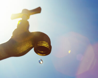 A single droplet falls from a faucet, symbolizing water scarcity or drought.
