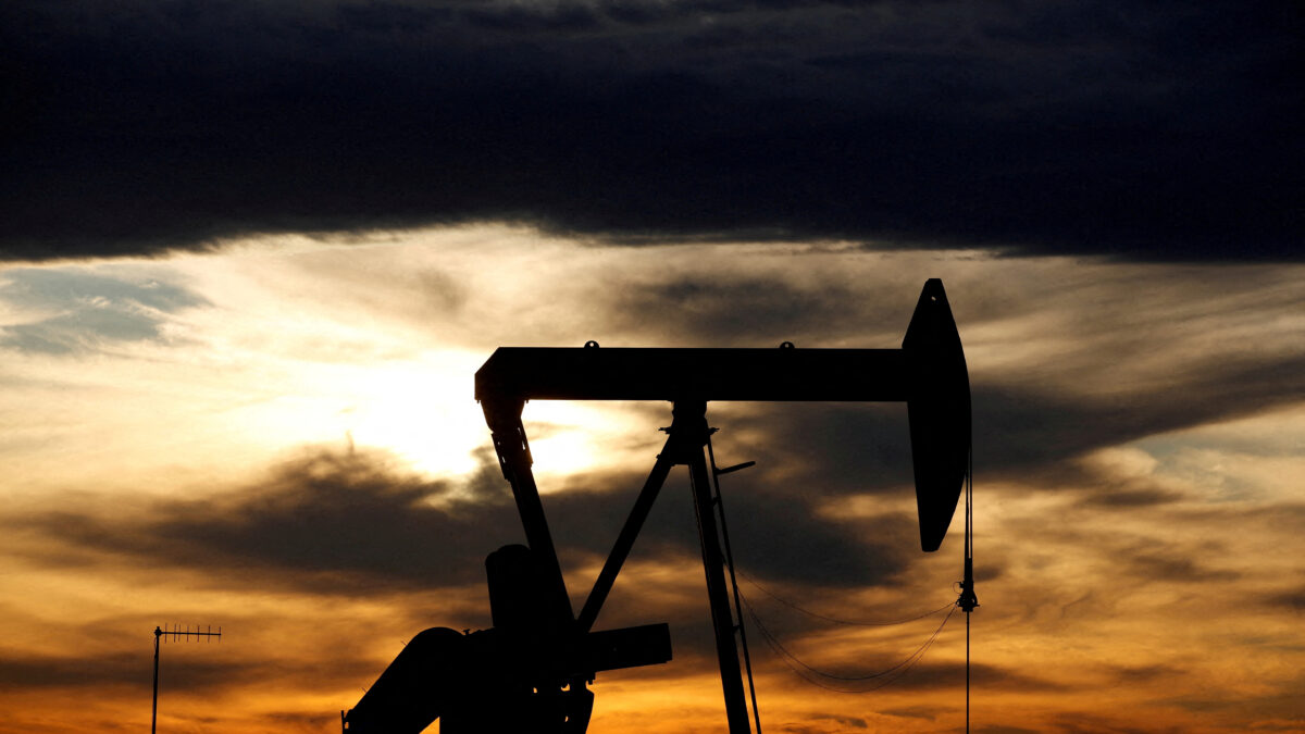 The sun sets behind a crude oil pump jack on a drill pad