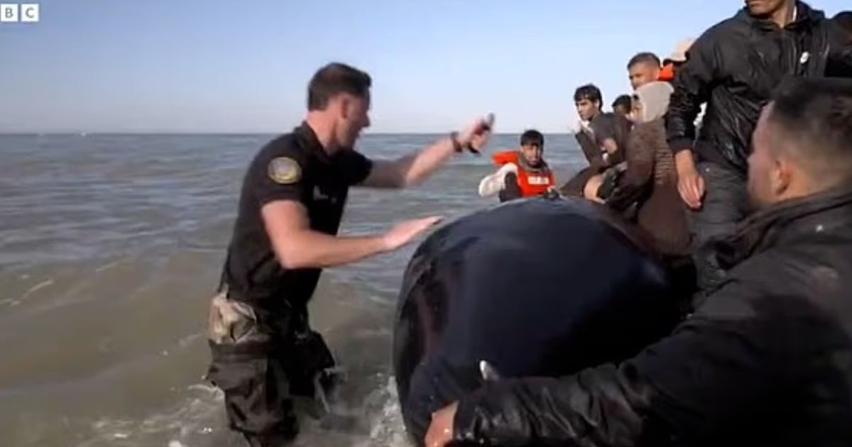 French policeman tears an inflatable boat with immigrants just before crossing the Channel to reach Britain