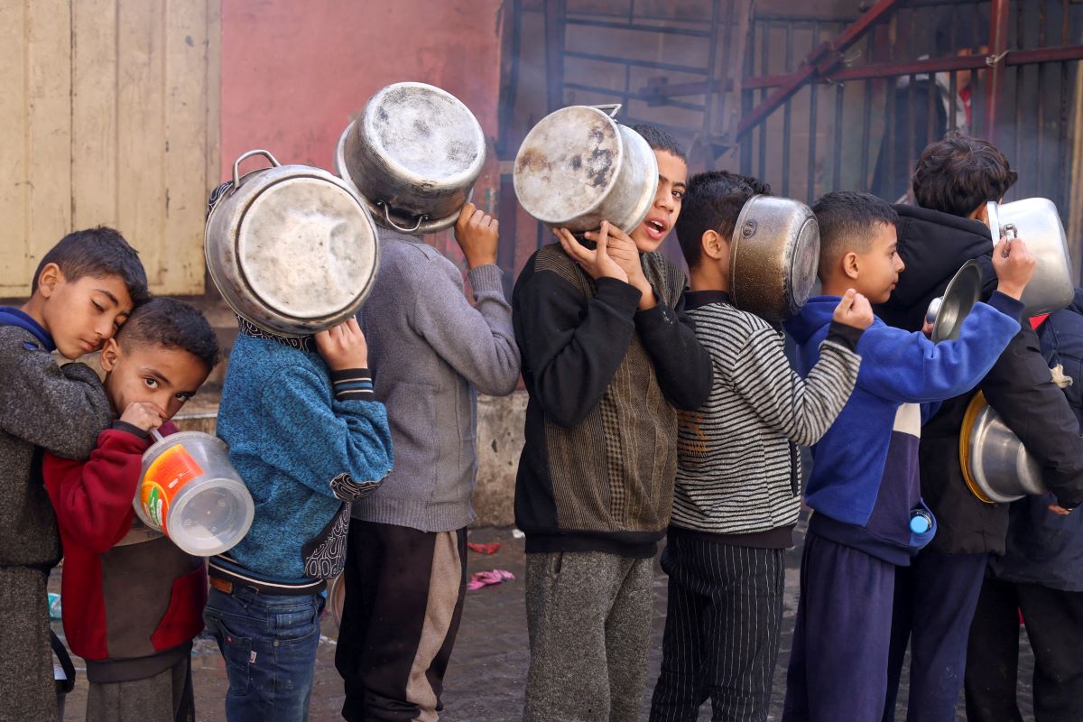 Kids hold pots as they wait in the queue to get food from charity