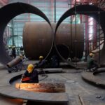 A worker cuts a metal plate inside an industrial tank manufacturing factory