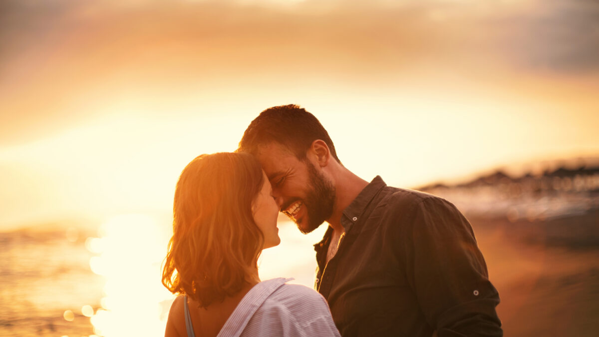 Young couple looking each other on the beach at late sunset. Love is in the air. They are about to kiss.