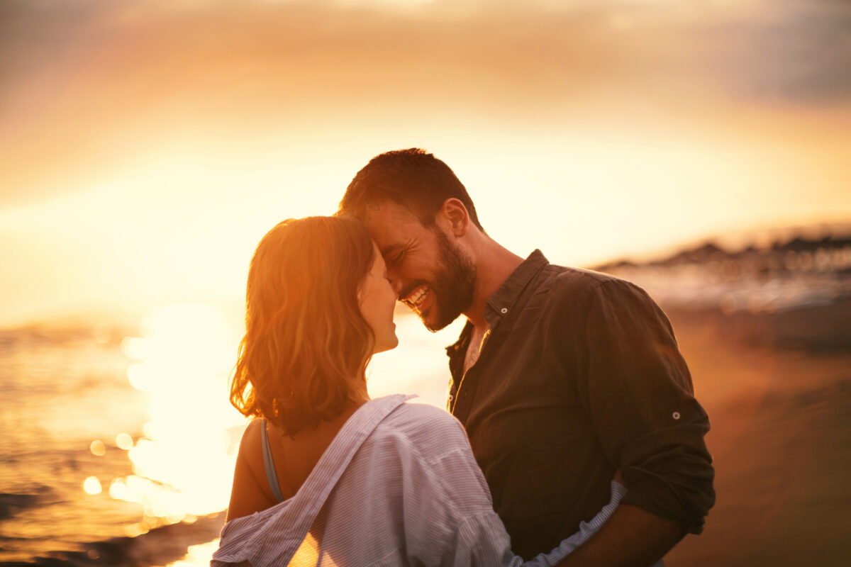 Young couple looking each other on the beach at late sunset. Love is in the air. They are about to kiss.
