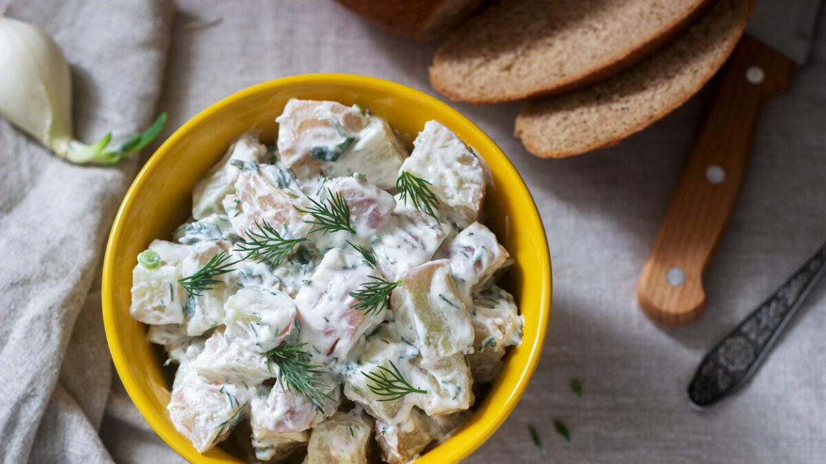 Traditional cold potato salad with onions and herbs on a linen tablecloth background. Rustic style, selective focus