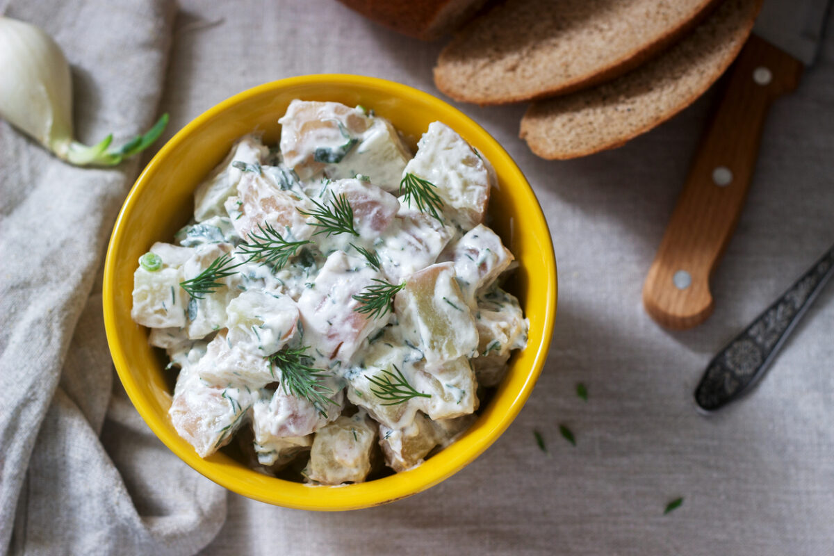 Traditional cold potato salad with onions and herbs on a linen tablecloth background. Rustic style, selective focus
