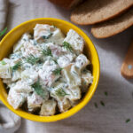 Traditional cold potato salad with onions and herbs on a linen tablecloth background. Rustic style, selective focus