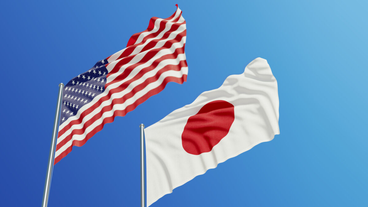 American and Japanese flags are waving with wind over blue sky.