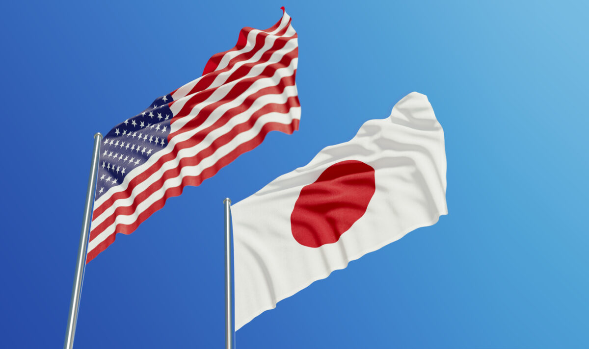 American and Japanese flags are waving with wind over blue sky.
