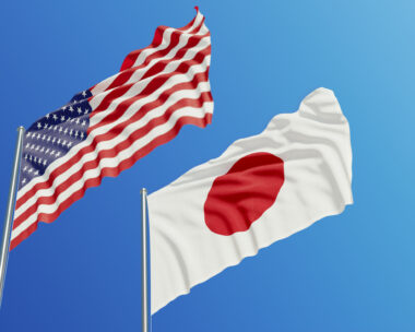 American and Japanese flags are waving with wind over blue sky.