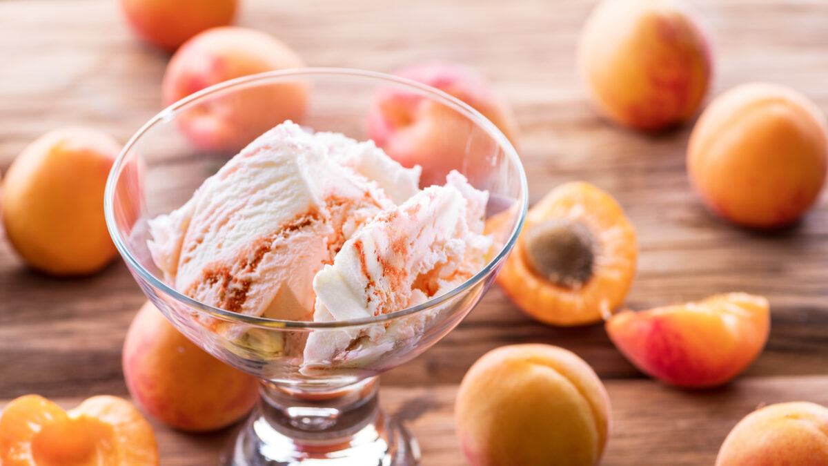 Homemade ice cream with apricot jam on the wooden table. Several apricots are near dessert bowl