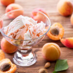 Homemade ice cream with apricot jam on the wooden table. Several apricots are near dessert bowl