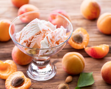 Homemade ice cream with apricot jam on the wooden table. Several apricots are near dessert bowl