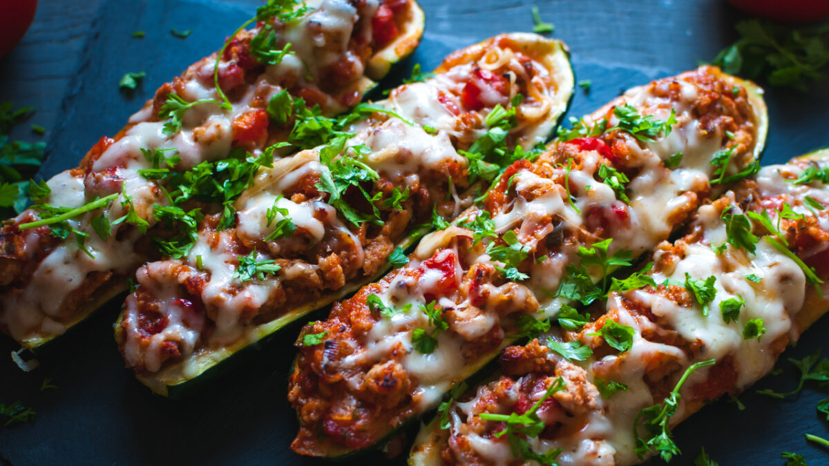 Homemade stuffed zucchini boats with ground beef, spicy tomato sauce, cheese and fresh parsley, on dark background