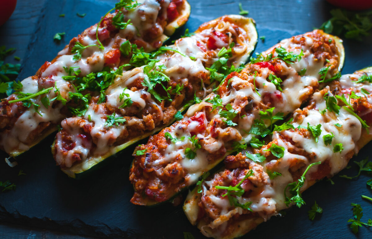 Homemade stuffed zucchini boats with ground beef, spicy tomato sauce, cheese and fresh parsley, on dark background