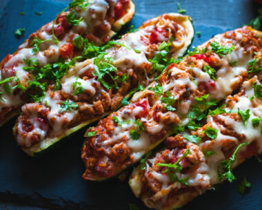 Homemade stuffed zucchini boats with ground beef, spicy tomato sauce, cheese and fresh parsley, on dark background